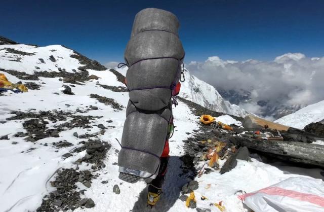 Gelje Sherpa carrying rescued climber on his back, wrapped in sleeping mat